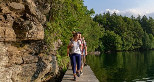 A group of hikers cross a boardwalk while enjoying the trails set among the trees, rocks and lakes at Limberlost Forest and Wildlife Reserve in Muskoka.